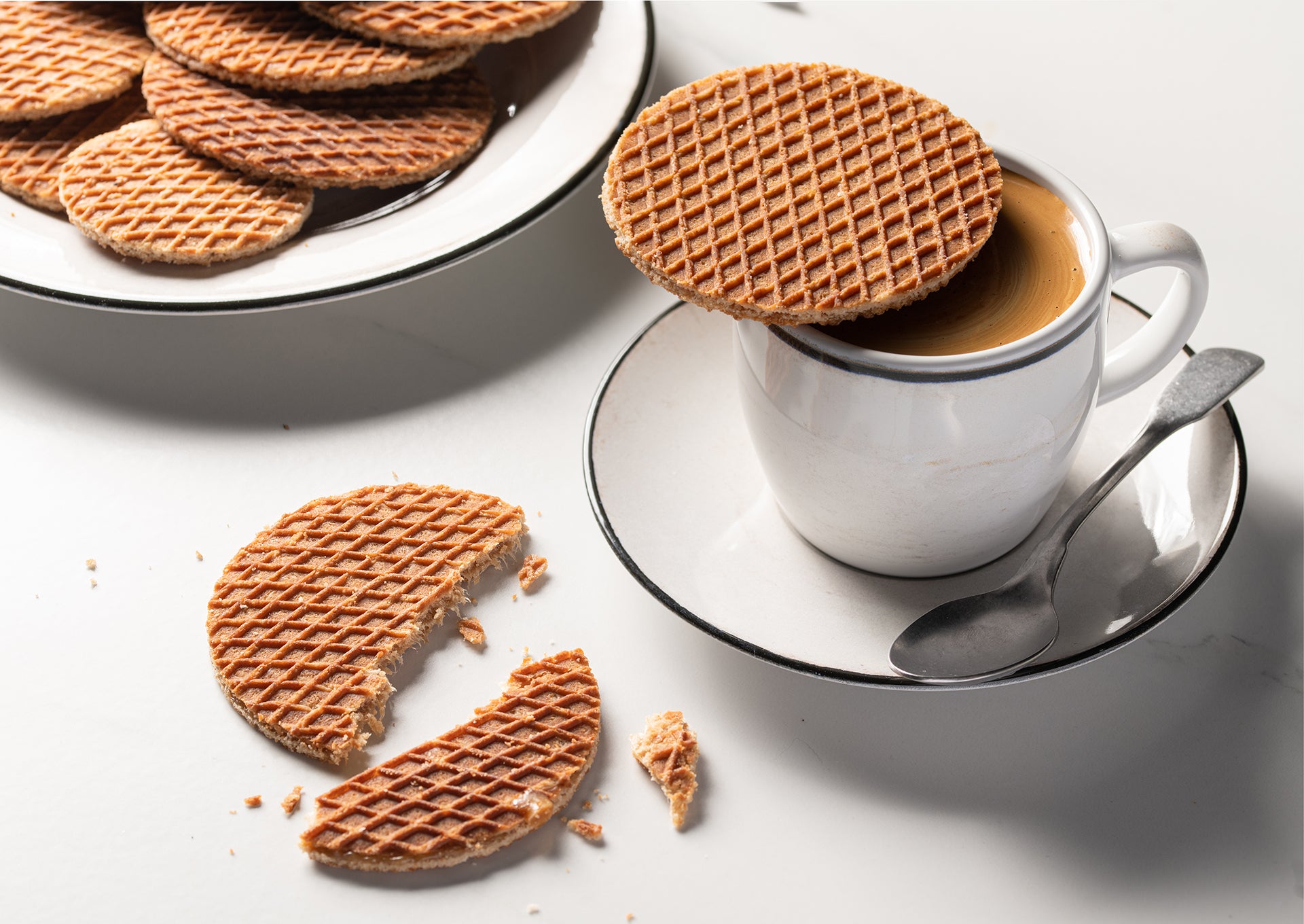 A cup of Wonderen Stroopwafels coffee and Wonderen Bundle 4x Stroopwafel 8 pack waffles on a white plate.